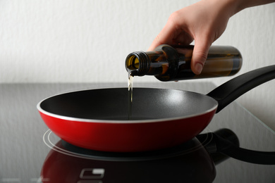 Photo of Woman pouring cooking oil from bottle into frying pan, closeup