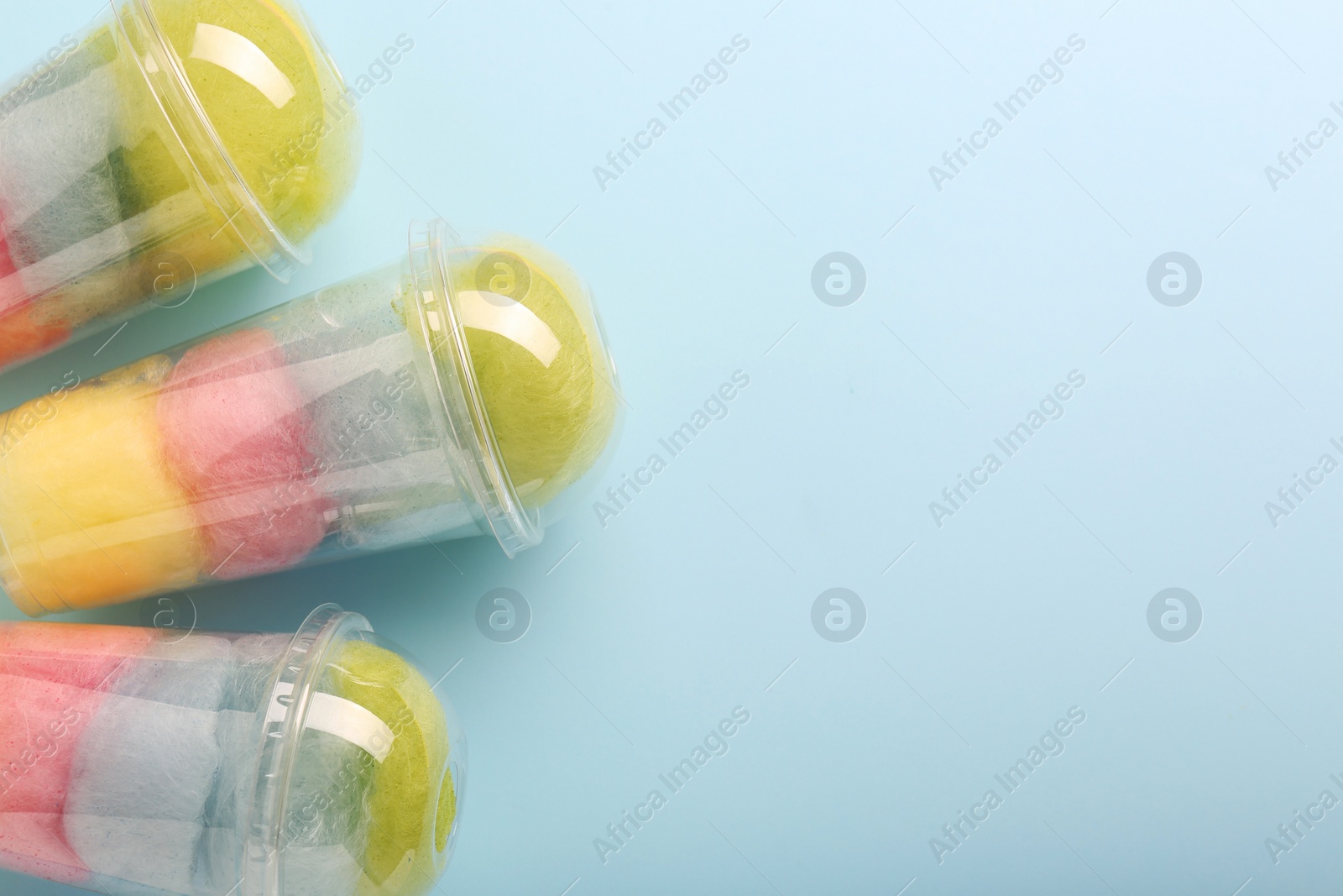 Photo of Colorful cotton candies in plastic cups on light blue background, flat lay. Space for text