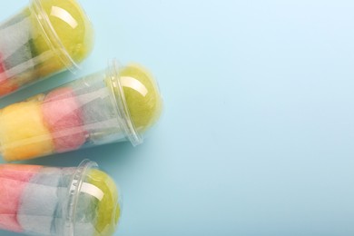 Colorful cotton candies in plastic cups on light blue background, flat lay. Space for text