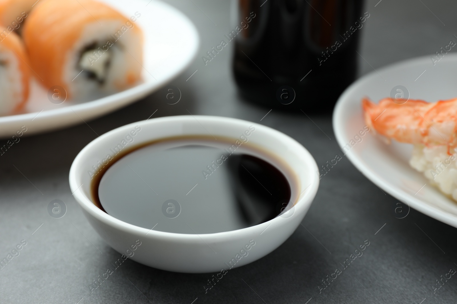 Photo of Bowl of tasty soy sauce on grey table, closeup