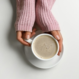 Photo of Woman holding cup of coffee at white table, top view. Space for text