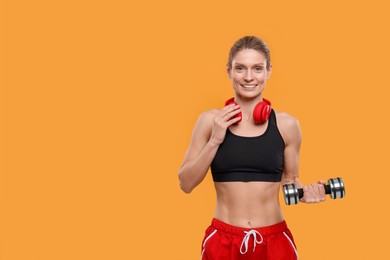 Sportswoman with dumbbell and headphones on yellow background, space for text