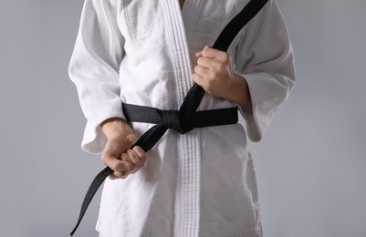 Photo of Martial arts master in keikogi with black belt on grey background, closeup