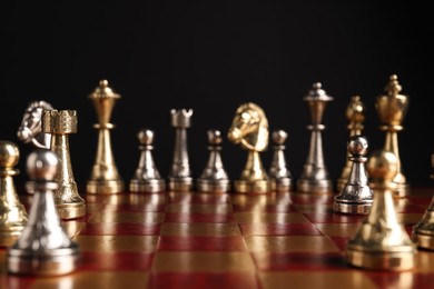 Photo of Many chess pieces on wooden checkerboard against black background, selective focus