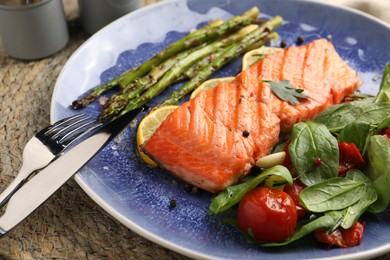 Photo of Tasty grilled salmon with tomatoes, asparagus, spinach and lemon served on table, closeup