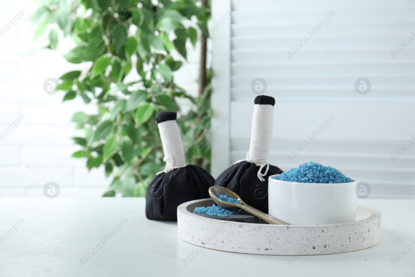 Photo of Blue sea salt and herbal bags on white table indoors, space for text