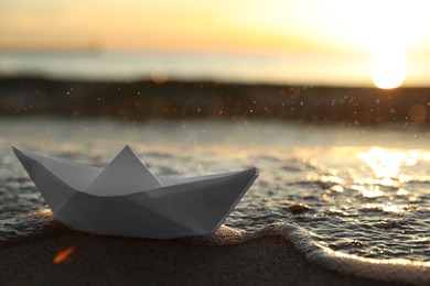 Photo of Sea wave carrying away white paper boat at sunset, space for text. Bokeh effect