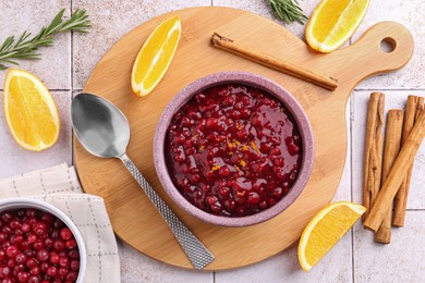 Tasty cranberry sauce in bowl and ingredients on white tiled table, flat lay