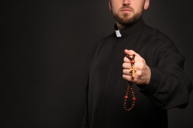 Priest with rosary beads on black background, closeup. Space for text