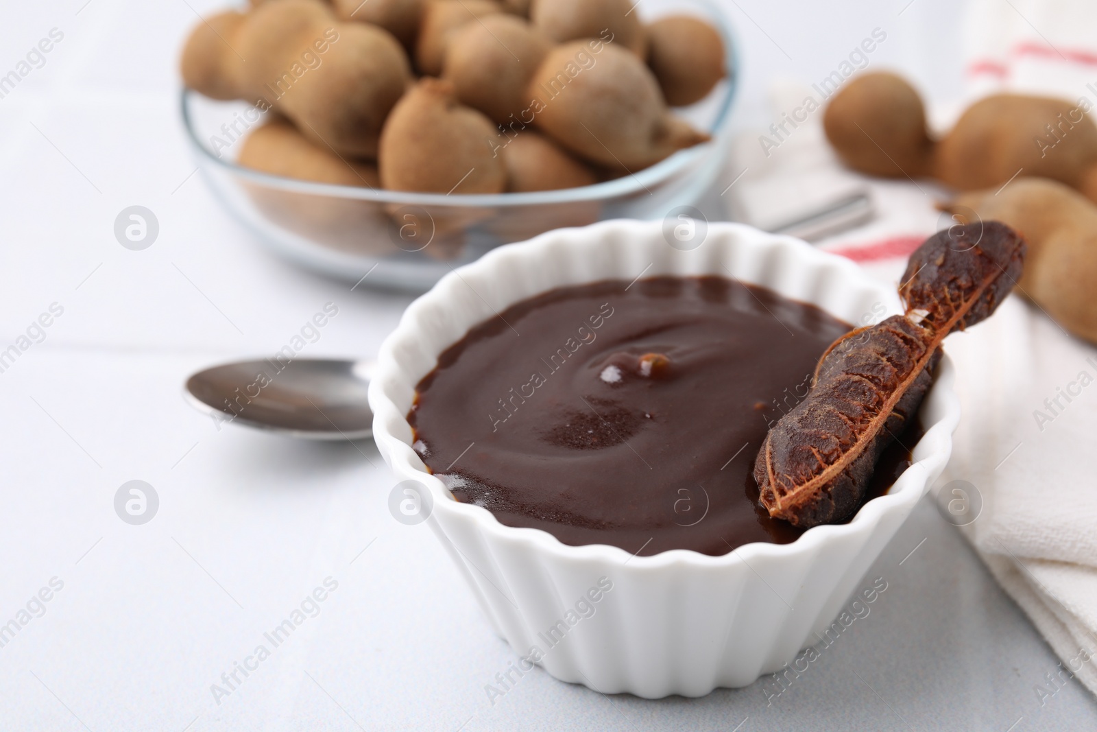 Bowl of tamarind sauce and fresh pods on light table, closeup Photo of Bowl of tamarind sauce and fresh pods on light table, closeup