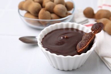 Photo of Bowl of tamarind sauce and fresh pods on light table, closeup