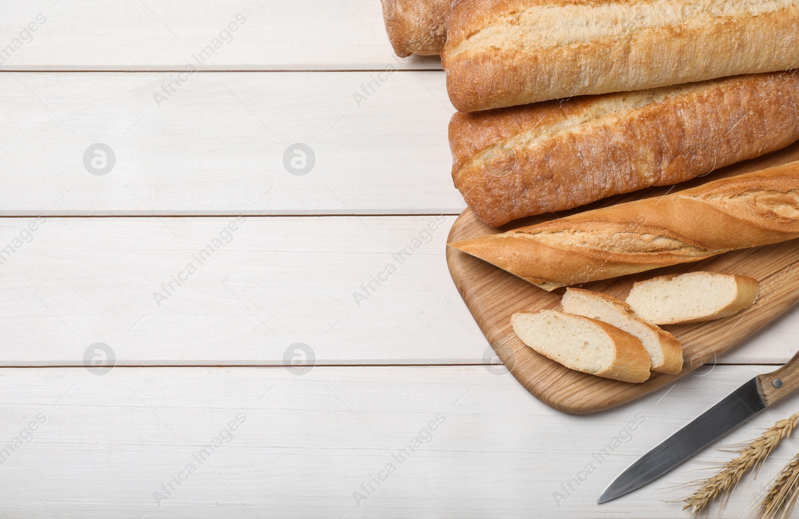 Photo of Fresh tasty baguettes, knife and spikelets on wooden table, flat lay. Space for text