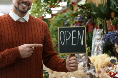 Photo of Male business owner holding OPEN sign in his flower shop, closeup
