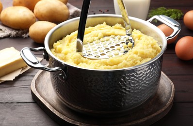 Photo of Mashing potatoes in pot on wooden table, closeup