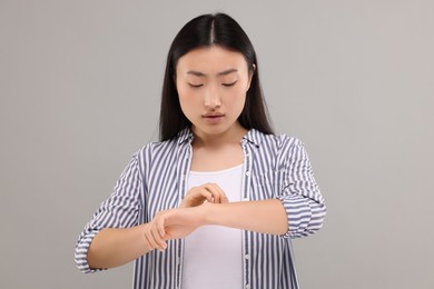 Photo of Suffering from allergy. Young woman scratching her arm on grey background