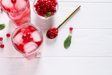 Photo of Tasty cranberry juice with ice cubes in glasses and fresh berries on white wooden table, flat lay. Space for text