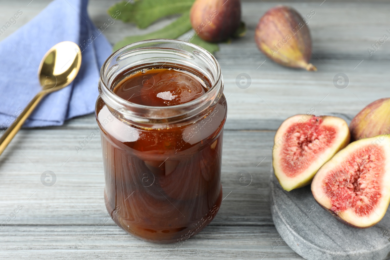 Photo of Jar of tasty sweet jam and fresh figs on grey table