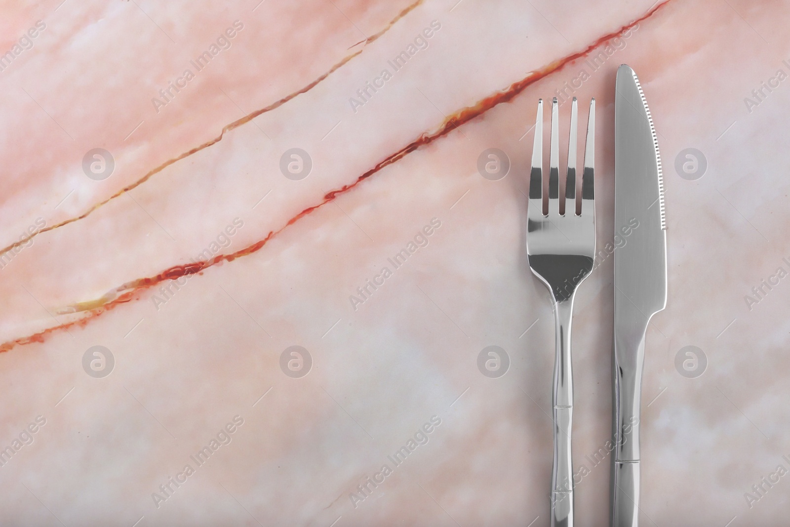 Photo of Shiny fork and knife on pink marble table, flat lay. Space for text
