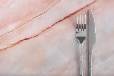 Photo of Shiny fork and knife on pink marble table, flat lay. Space for text