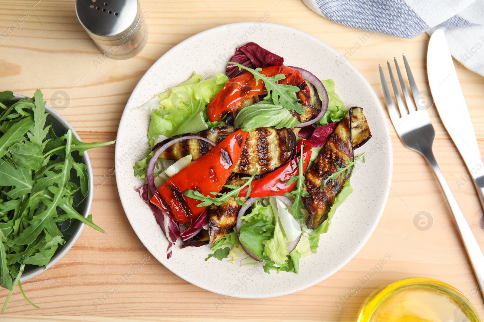 Photo of Delicious salad with roasted eggplant and arugula served on wooden table, flat lay