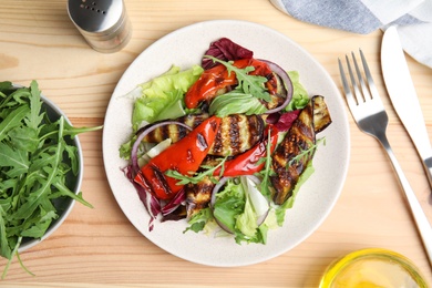 Photo of Delicious salad with roasted eggplant and arugula served on wooden table, flat lay