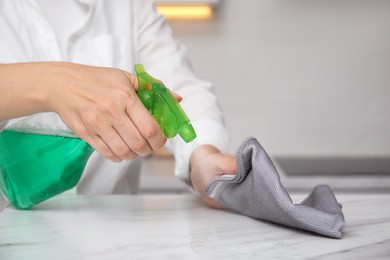 Photo of Woman cleaning white marble table with rag and detergent indoors, closeup