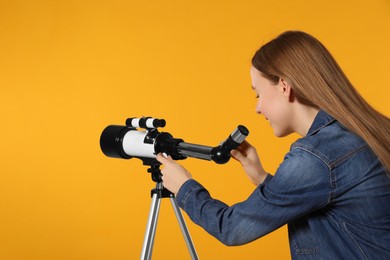 Photo of Young astronomer looking at stars through telescope on orange background