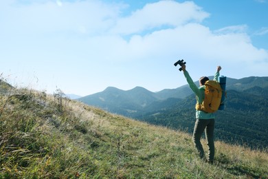 Happy tourist with hiking equipment and binoculars in mountains, back view