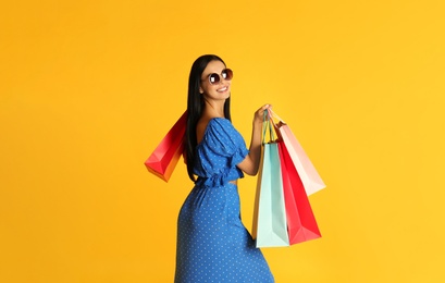 Beautiful young woman with paper shopping bags on yellow background