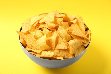 Photo of Tasty mexican nachos chips in metal bowl on yellow background