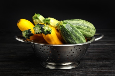 Colander with fresh ripe zucchini on black wooden table