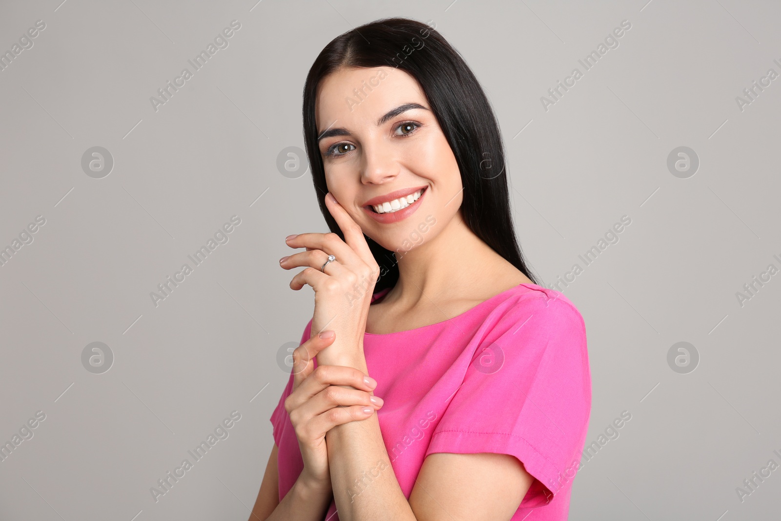 Photo of Happy young woman wearing beautiful engagement ring on grey background