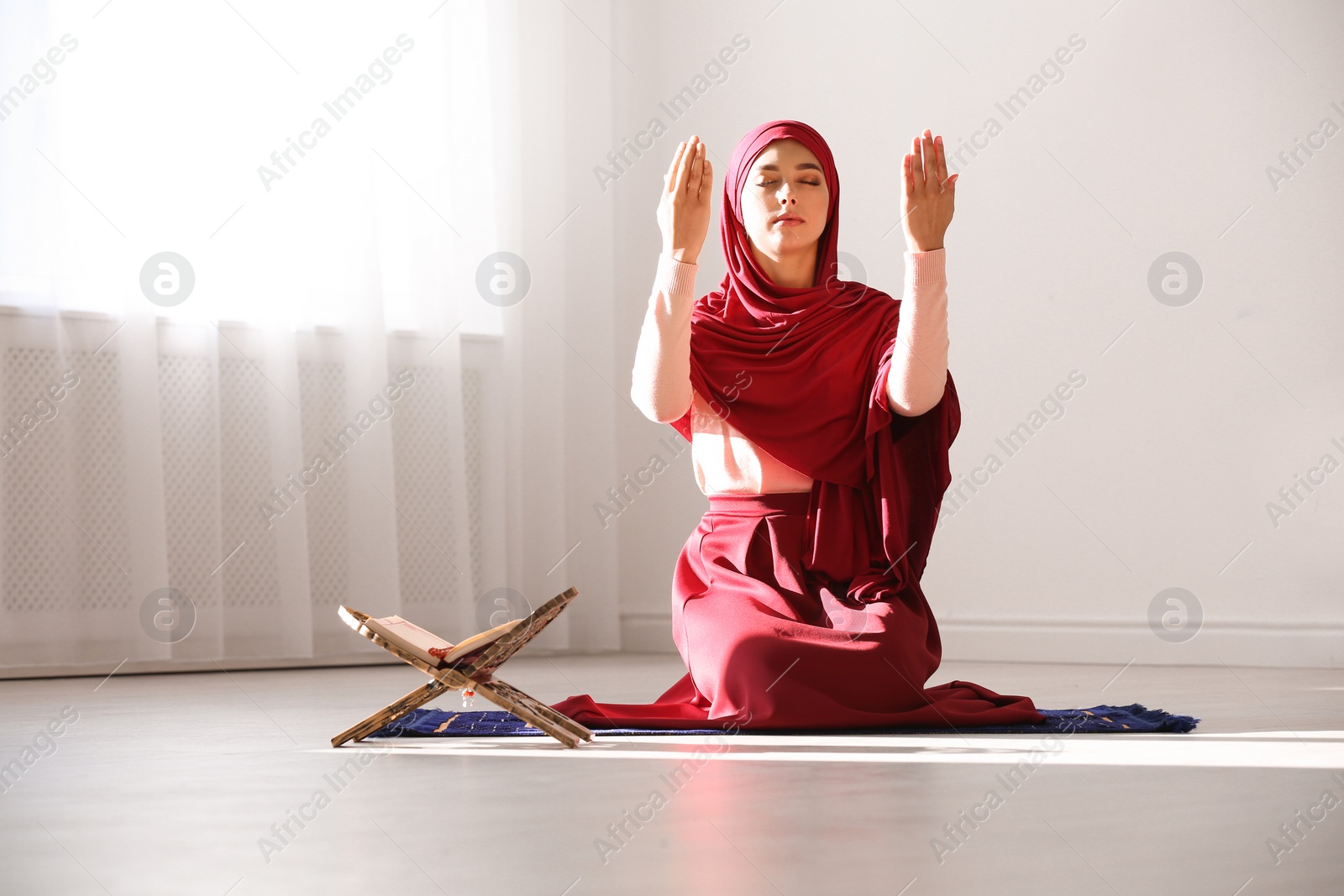 Photo of Muslim woman in hijab praying on mat indoors