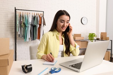 Photo of Seller talking on phone while working with laptop in office. Online store