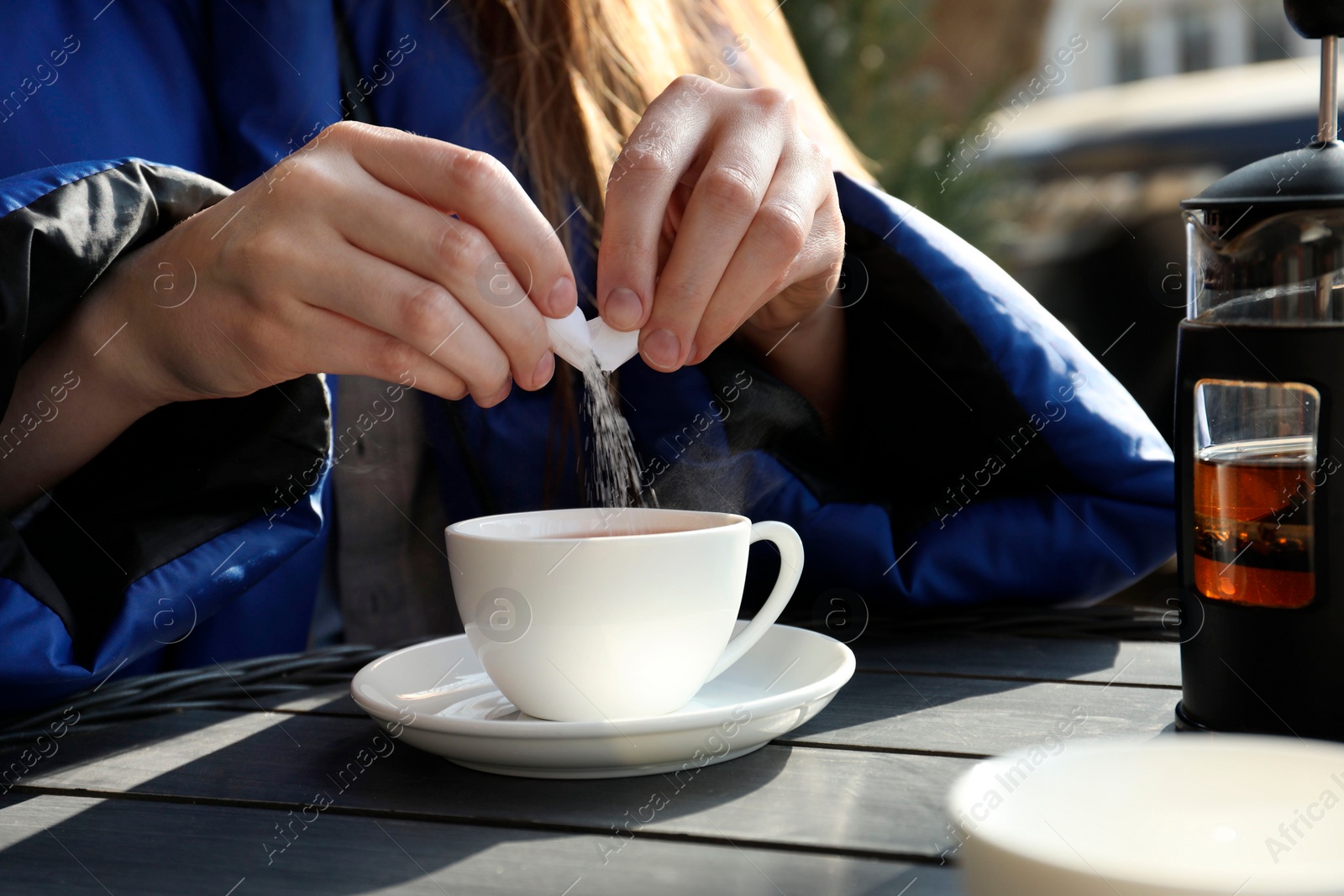 Photo of Woman adding sugar into cup of tea at black wooden table in outdoor cafe, closeup