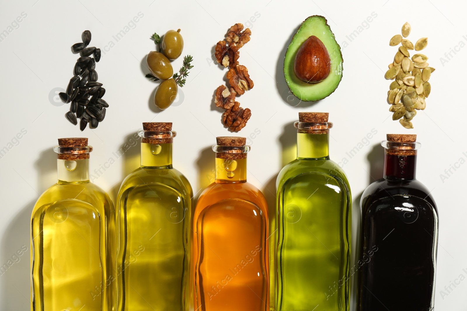 Photo of Vegetable fats. Different cooking oils in glass bottles and ingredients on white background, flat lay