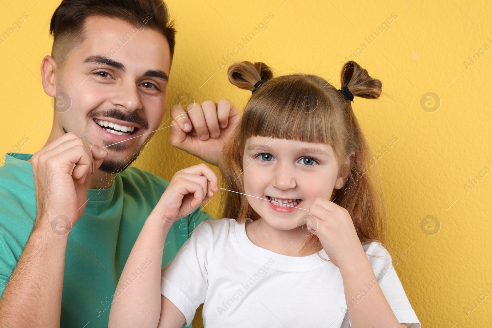 Photo of Little girl and her father flossing teeth on color background