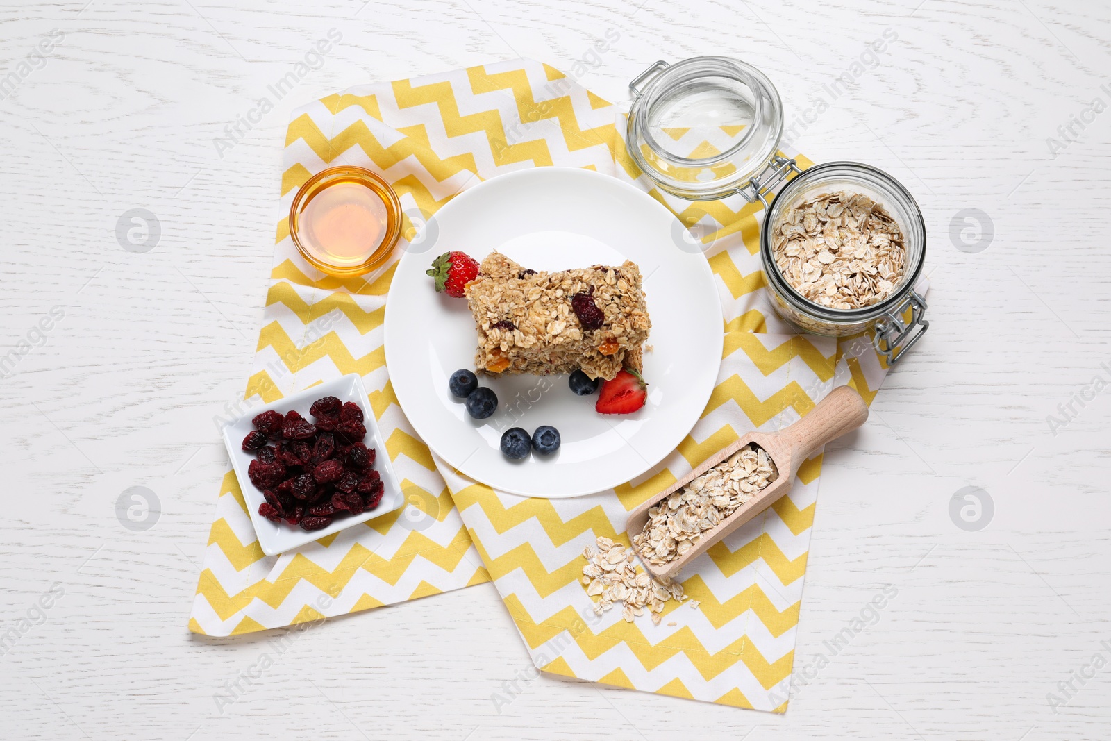 Photo of Tasty granola bars and ingredients on white wooden table, flat lay