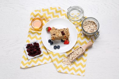 Photo of Tasty granola bars and ingredients on white wooden table, flat lay