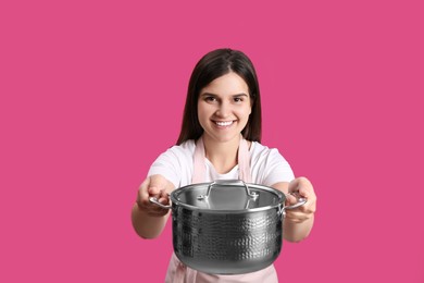 Happy young woman with cooking pot on pink background