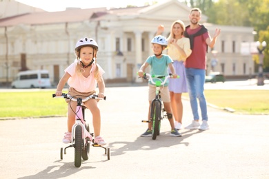 Happy parents teaching children to ride bicycles outdoors