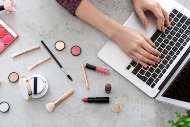 Photo of Young woman with makeup products using laptop at table. Beauty blogger