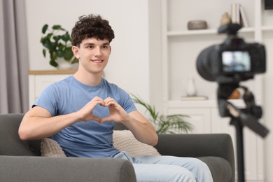 Photo of Smiling teenage blogger making heart gesture to his subscribers while streaming at home