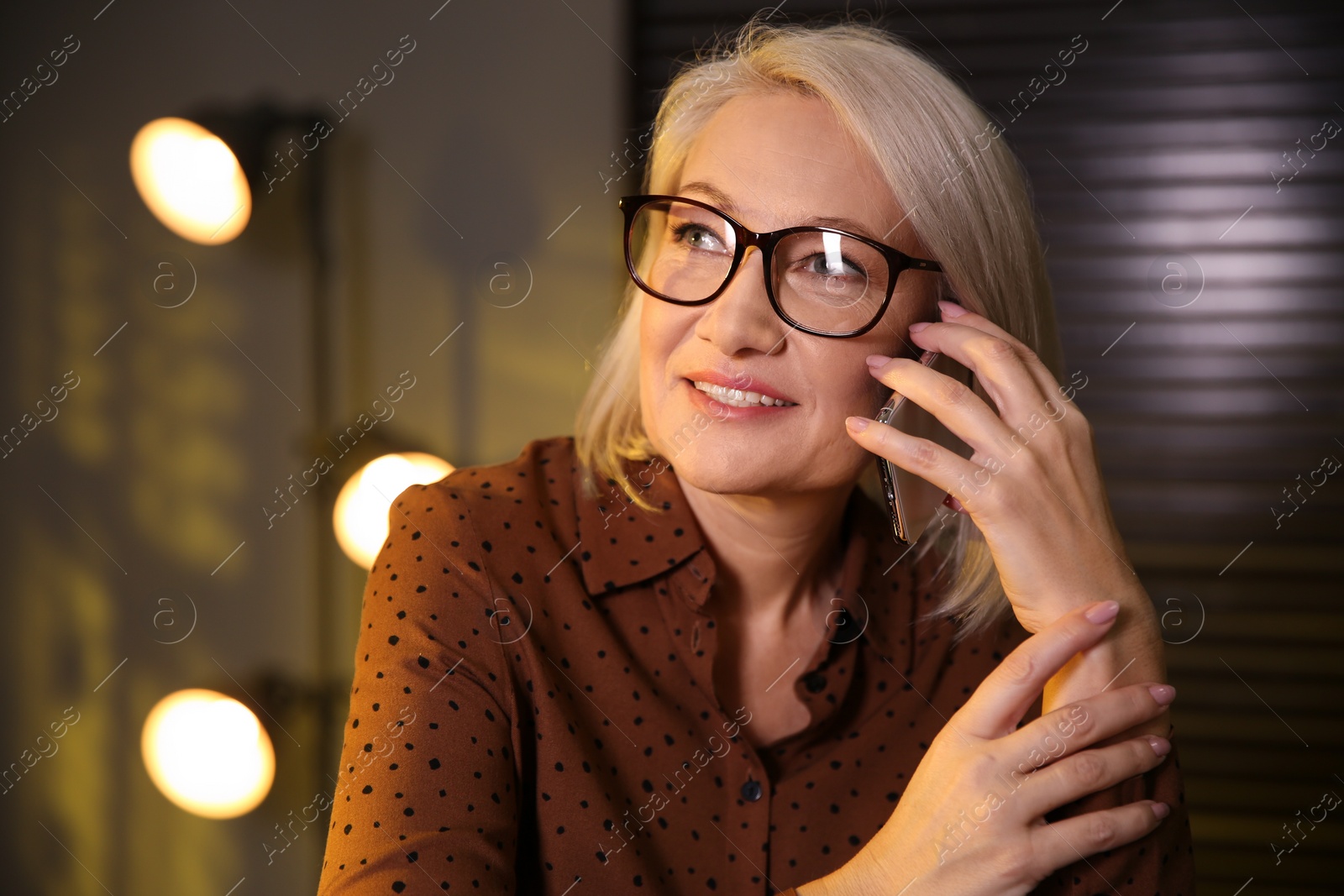 Photo of Beautiful mature woman in glasses talking on smartphone indoors