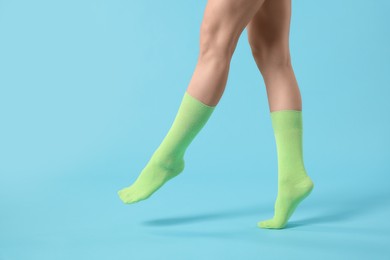 Woman in stylish lime socks on light blue background, closeup. Space for text