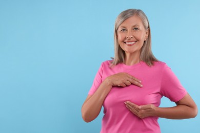 Photo of Beautiful senior woman doing breast self-examination on light blue background, space for text