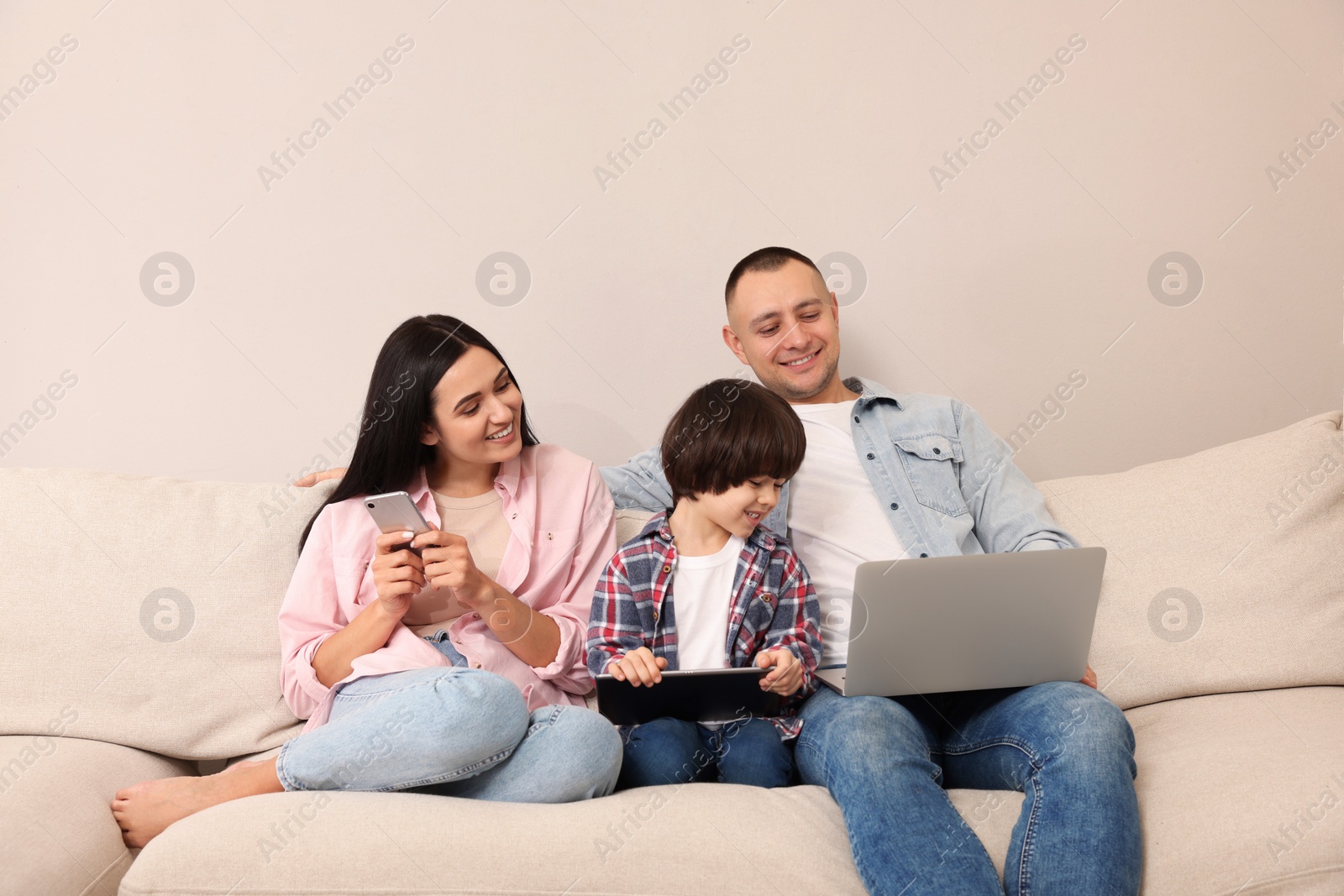 Photo of Happy family with gadgets on sofa at home