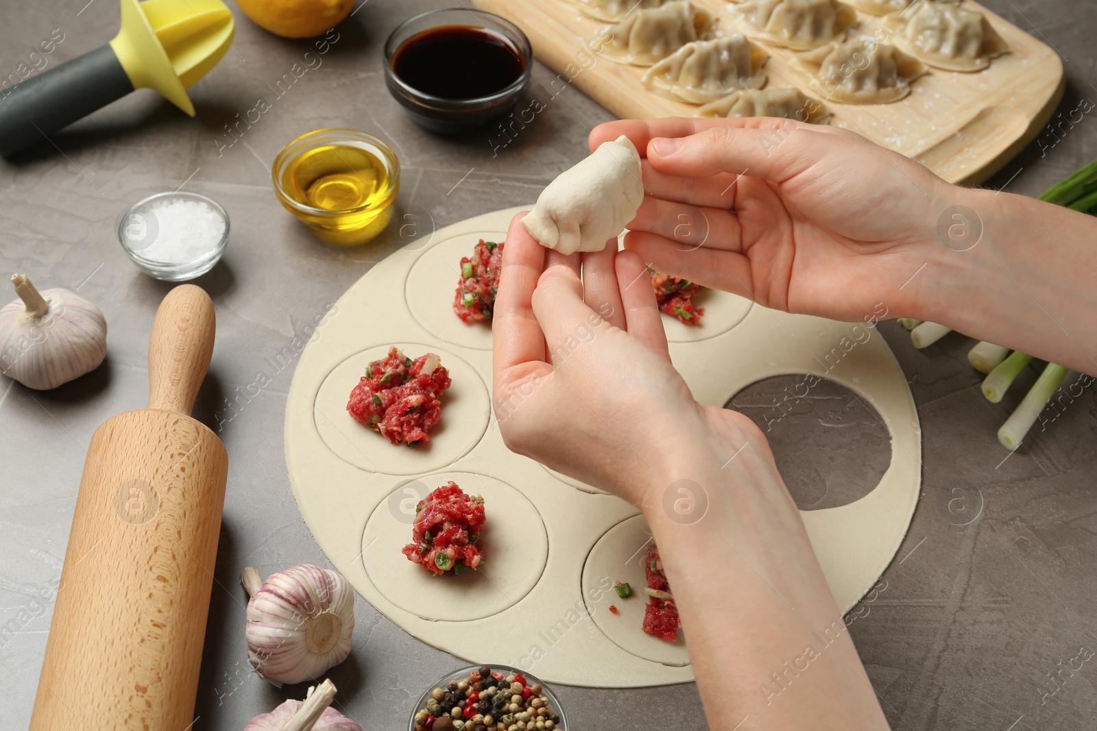 Photo of Woman cooking delicious gyoza at light grey table, closeup