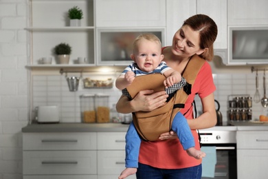 Photo of Woman with her son in baby carrier at home. Space for text