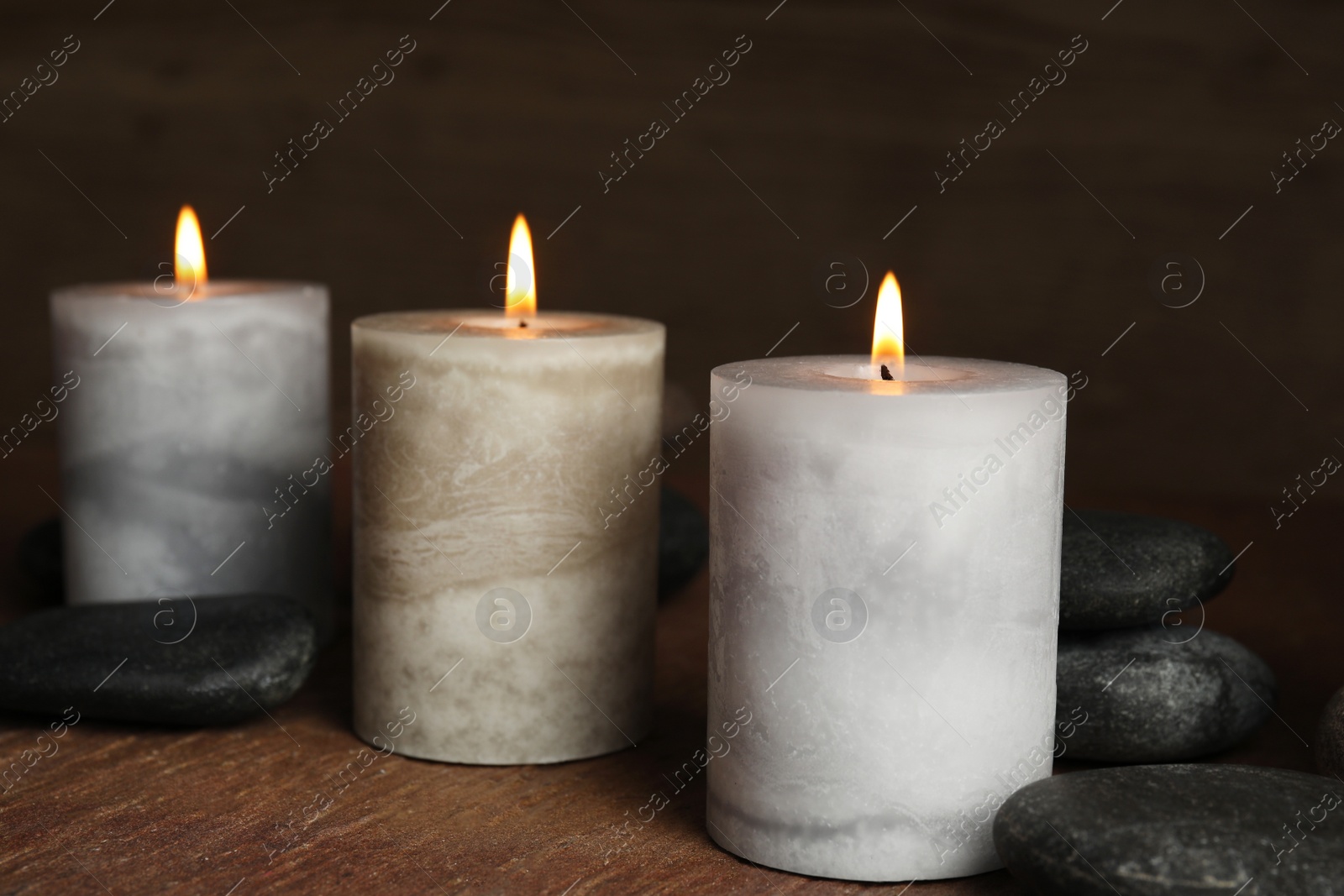 Photo of Burning candles and spa stones on wooden table